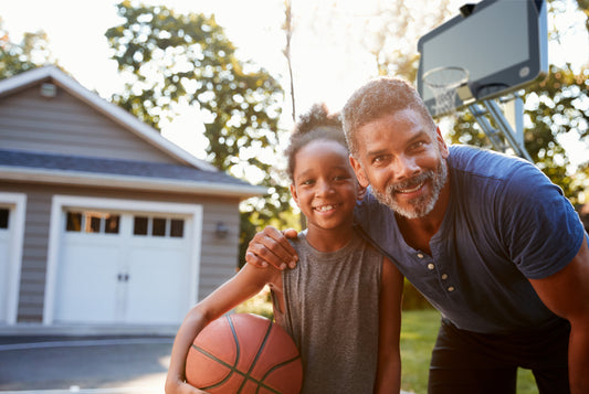 A father smiling with his daughter who is holding a basketball